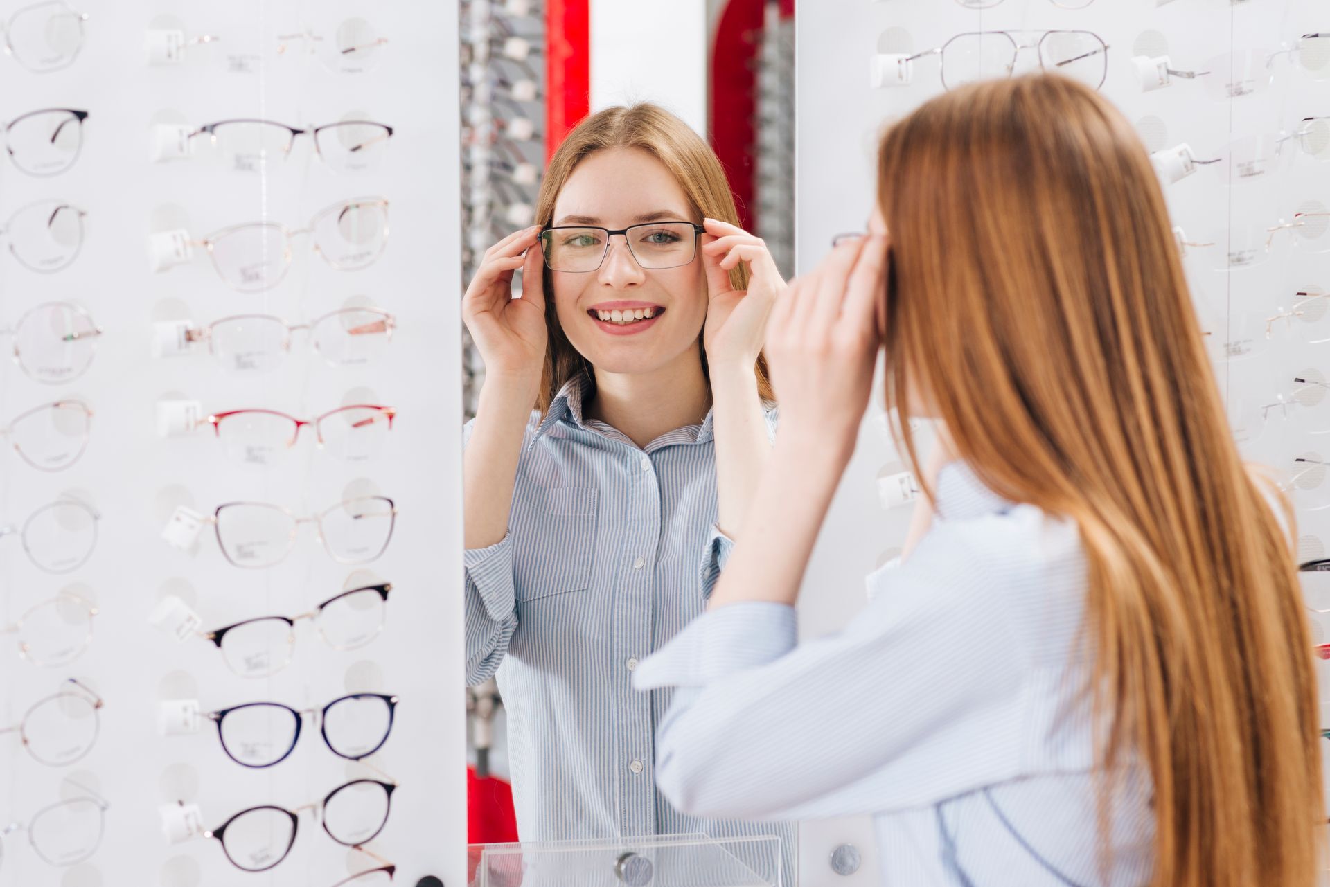 A woman is trying on glasses in front of a mirror in an optical shop.