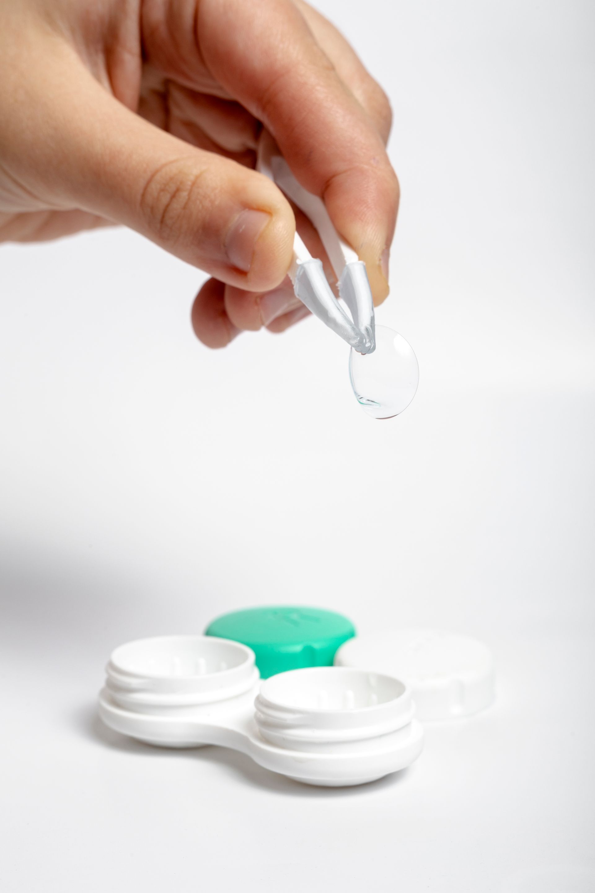 A person is holding a pair of tweezers over a contact lens case.