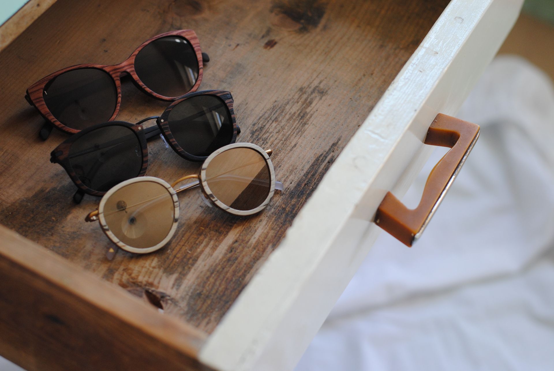 Three pairs of sunglasses are sitting in a wooden drawer.