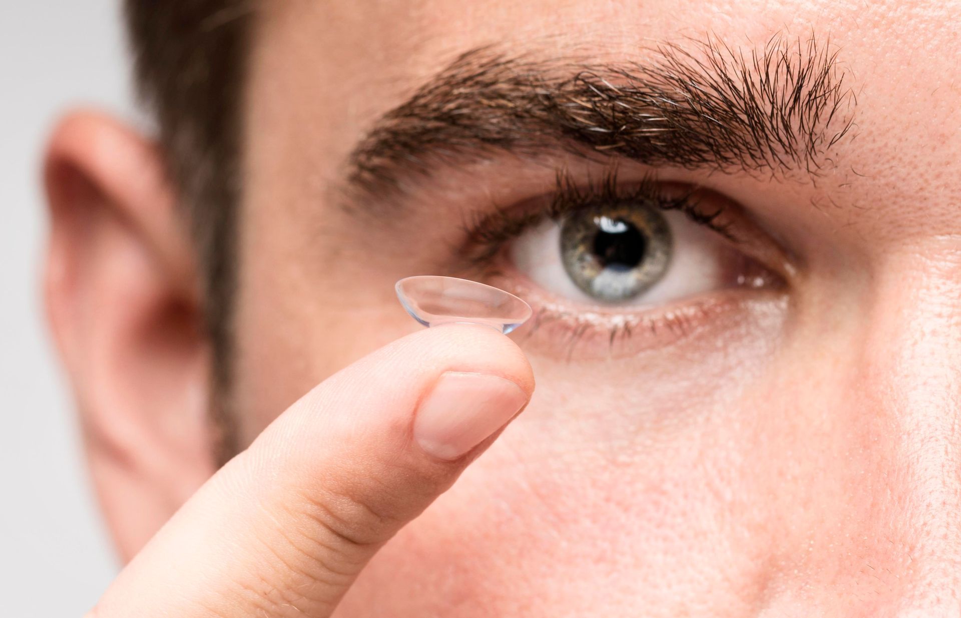 Man putting in a contact lens. Close-up of eye with blue iris, finger holding a clear lens.