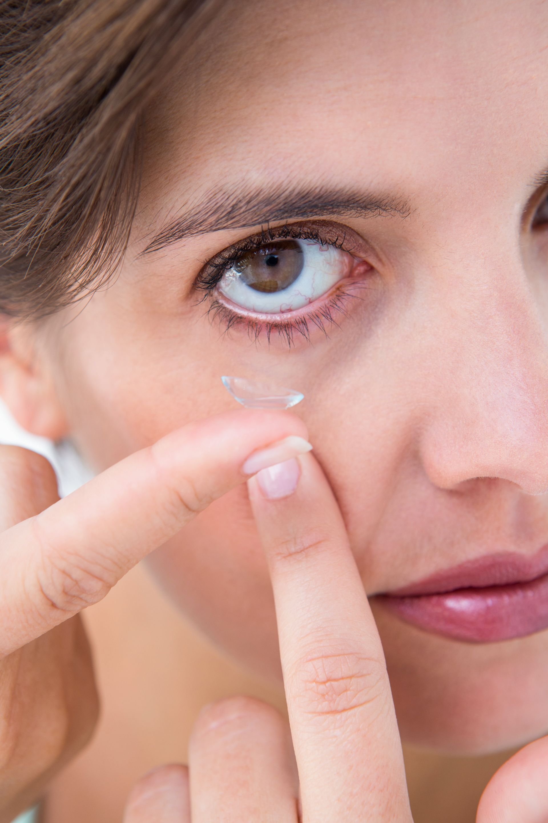 A woman is putting a contact lens in her eye.