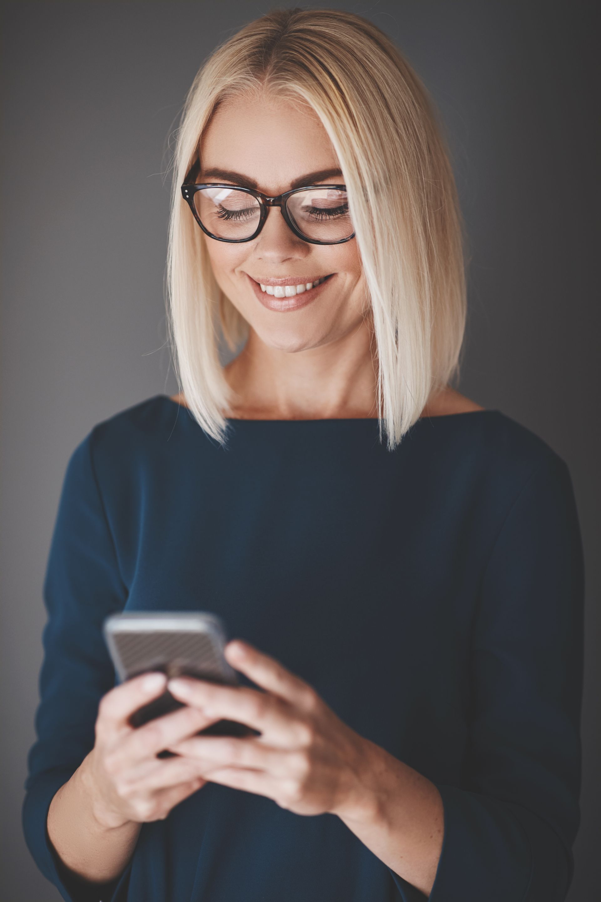 A woman wearing glasses is looking at her cell phone.