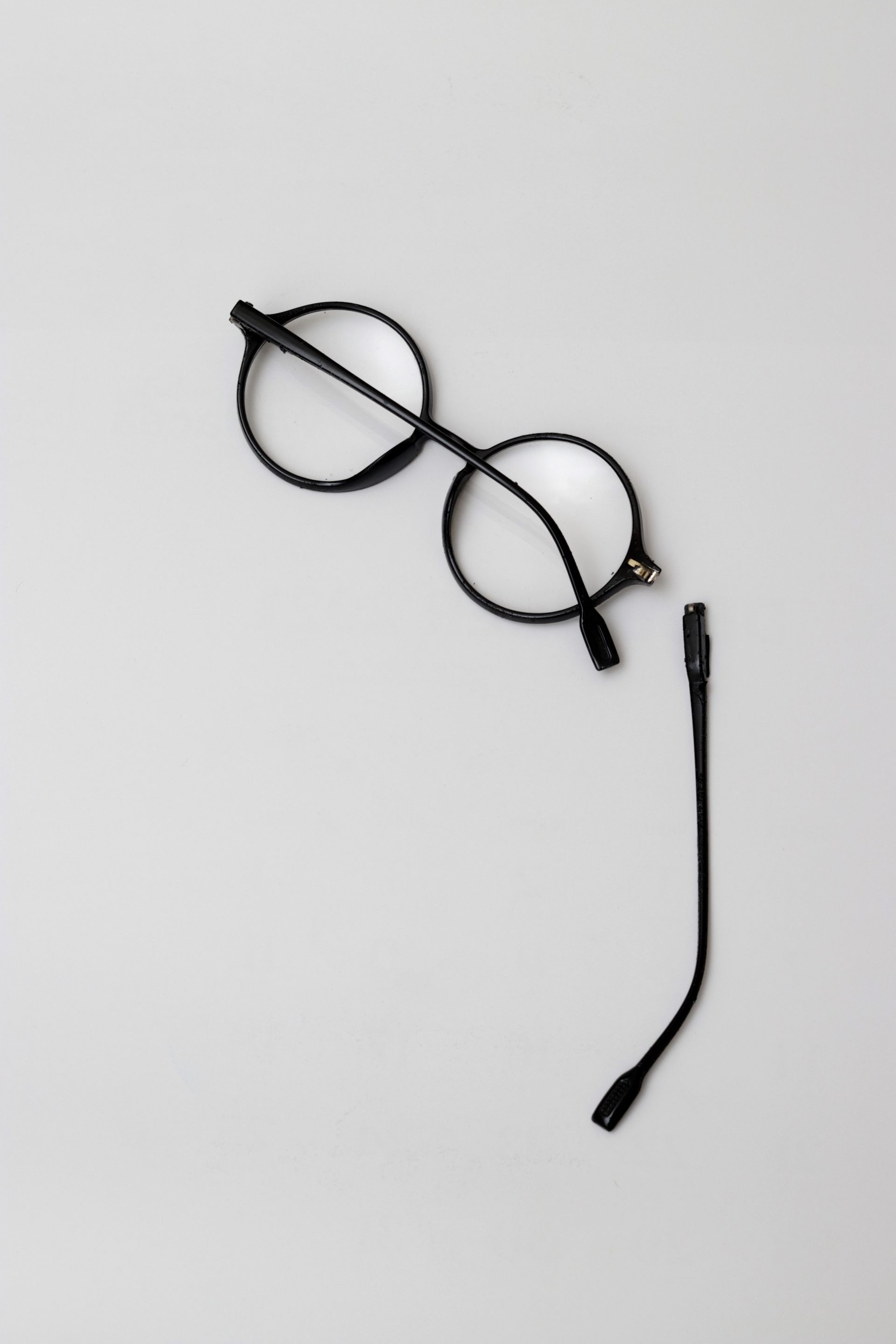 A pair of glasses with a broken arm on a white surface.