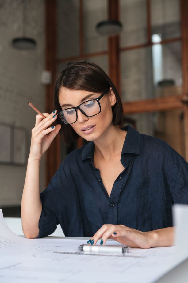 A woman wearing glasses is sitting at a table with a clipboard.