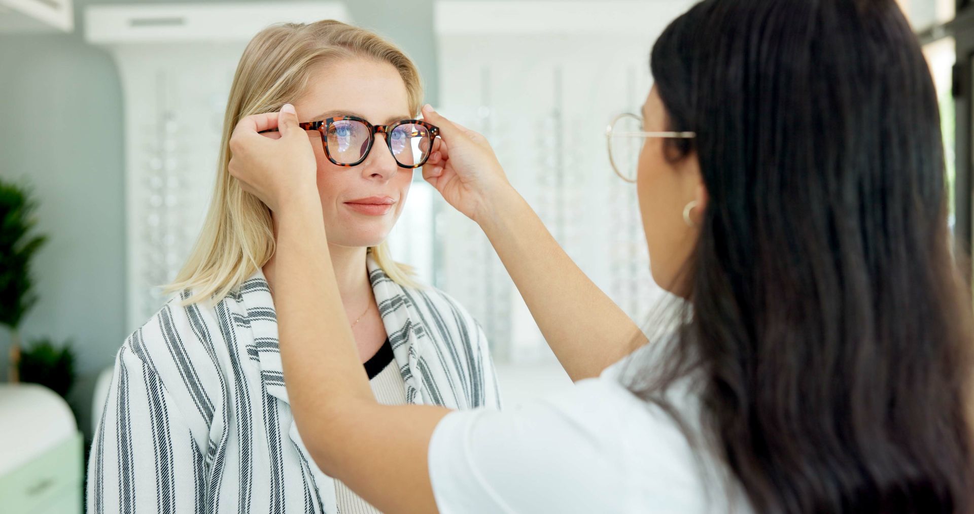 A woman is trying on glasses with an optician in a store.