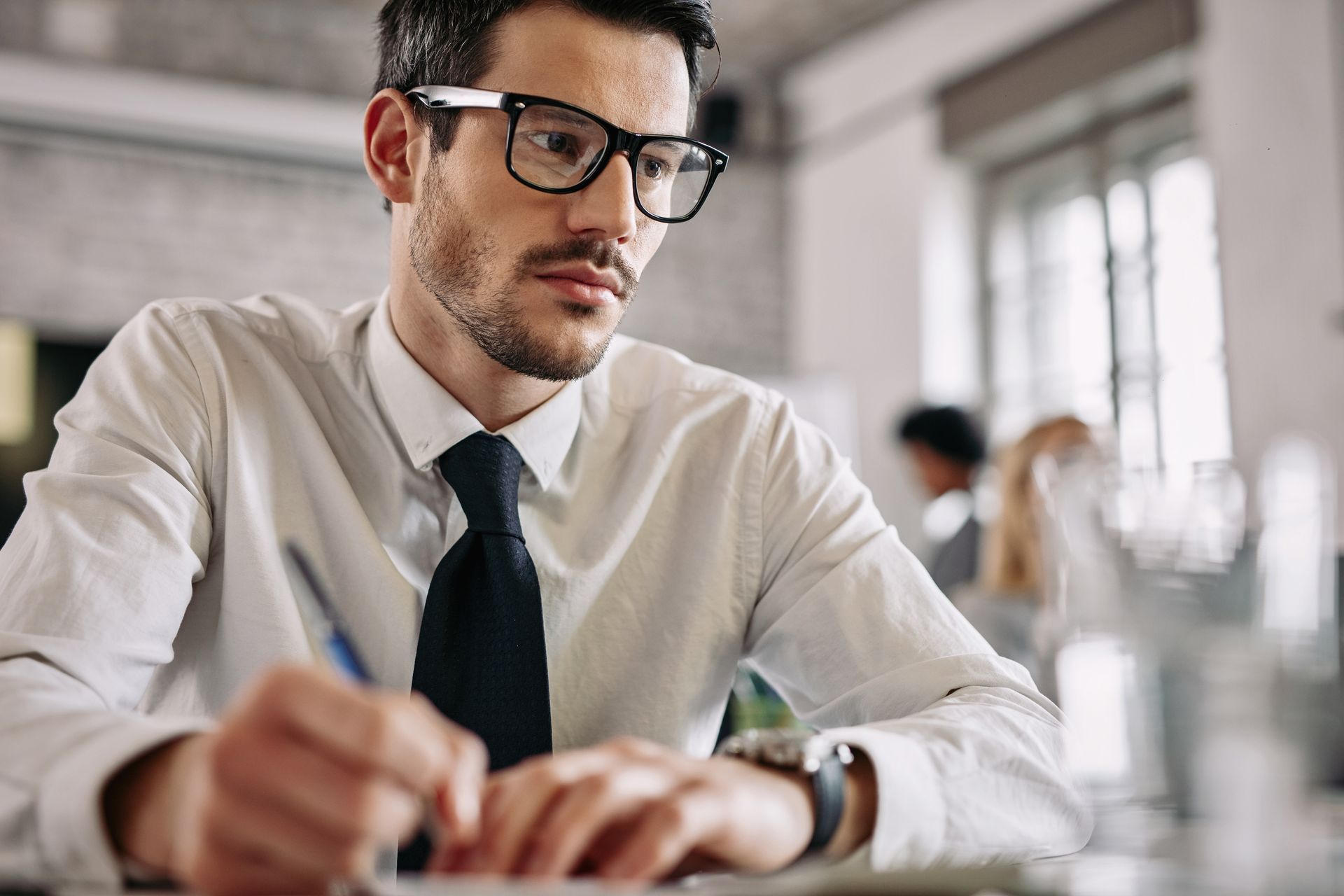 A man wearing glasses and a tie is sitting at a desk.