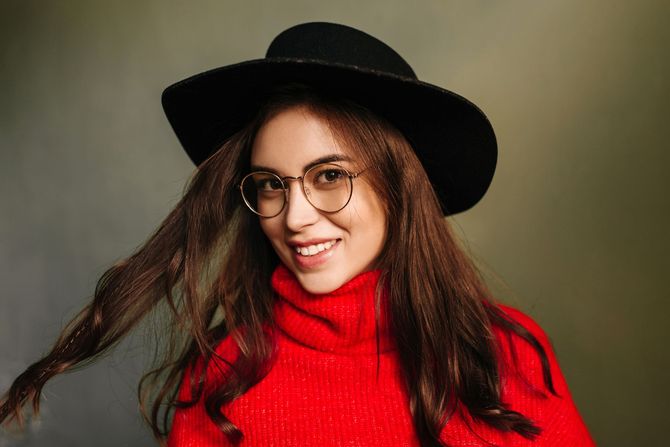 A woman wearing a hat and glasses is smiling.