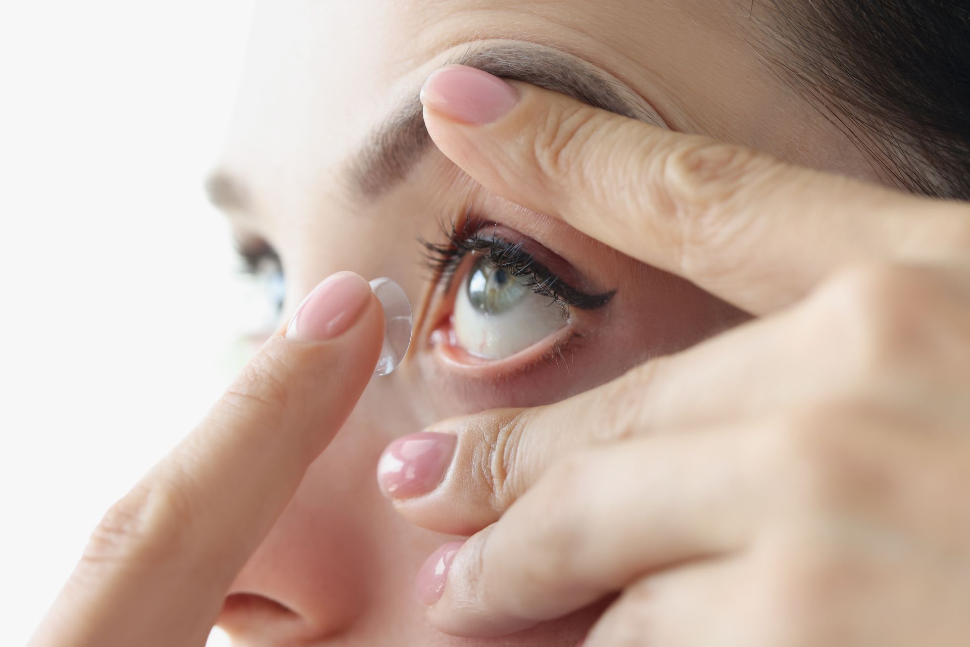 A woman is putting a contact lens in her eye.