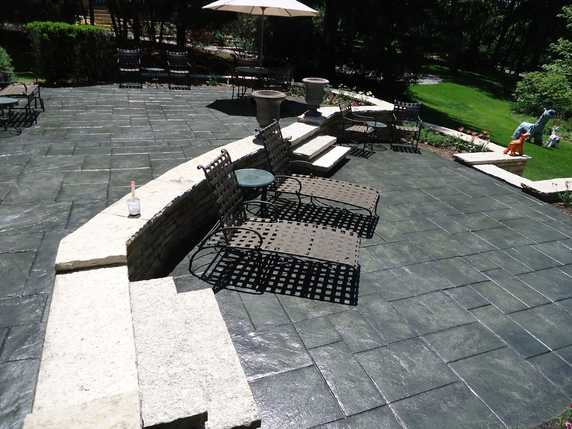 Stone patio with curved white bench, picnic tables, and a grassy park area in sunlight