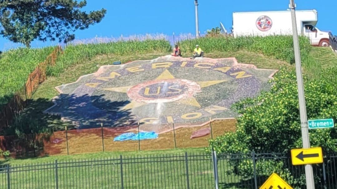 Hillside mural with a large compass design, green grass, and a yellow arrow sign in front