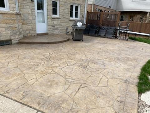 Stone patio with stamped concrete, a house wall, grill, and outdoor seating area.