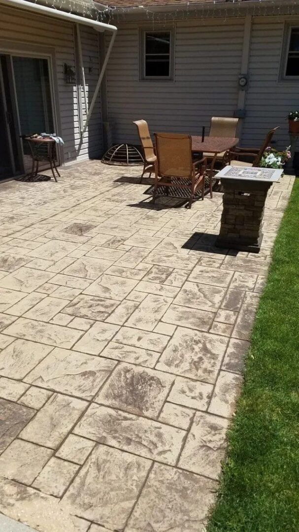 Back patio with patio table and chairs on patterned concrete beside a strip of grass
