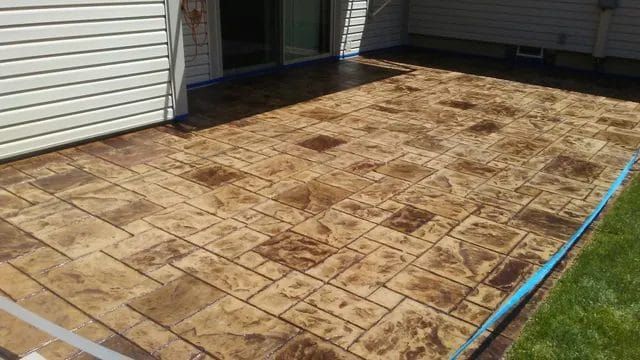 Stamped concrete patio beside a house, with a tan and brown stone pattern and blue edging strip