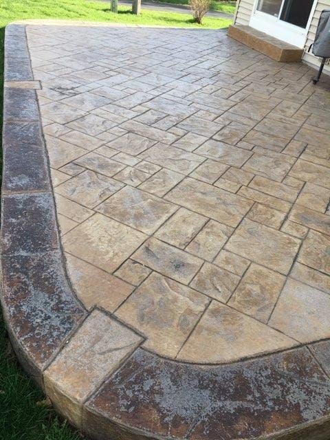 Stamped concrete patio with a curved stone border and tan patterned surface by a house.