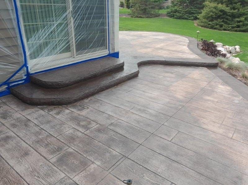 Wooden deck with a curved step beside a screened patio and a grassy yard with shrubs