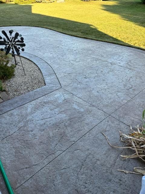 Stamped concrete patio beside a green lawn, with a small wind spinner and garden hose visible.