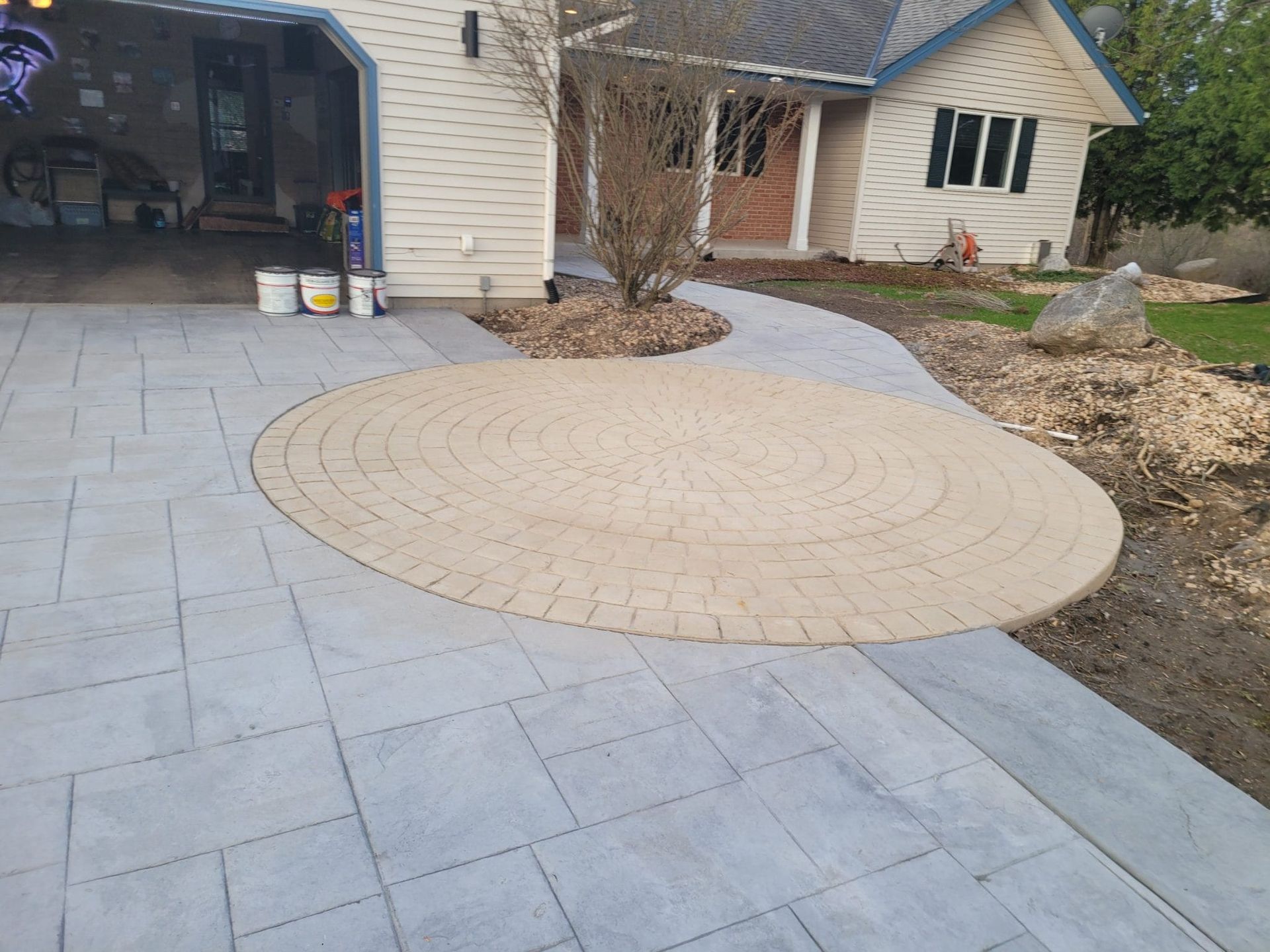 Backyard patio with large gray pavers and a circular tan stone inlay beside a house