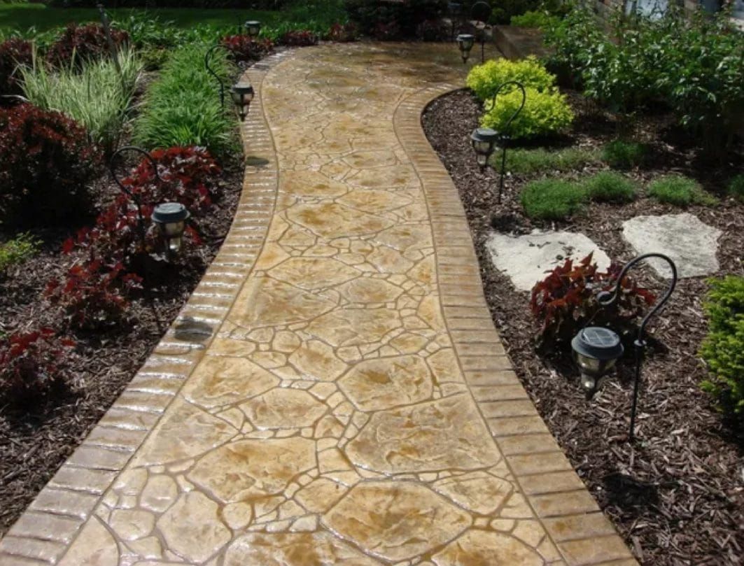 Curved tan stone garden path bordered by mulch, red plants, and greenery