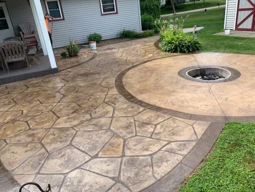 Stamped concrete patio with a circular fire pit beside a grassy yard and house porch