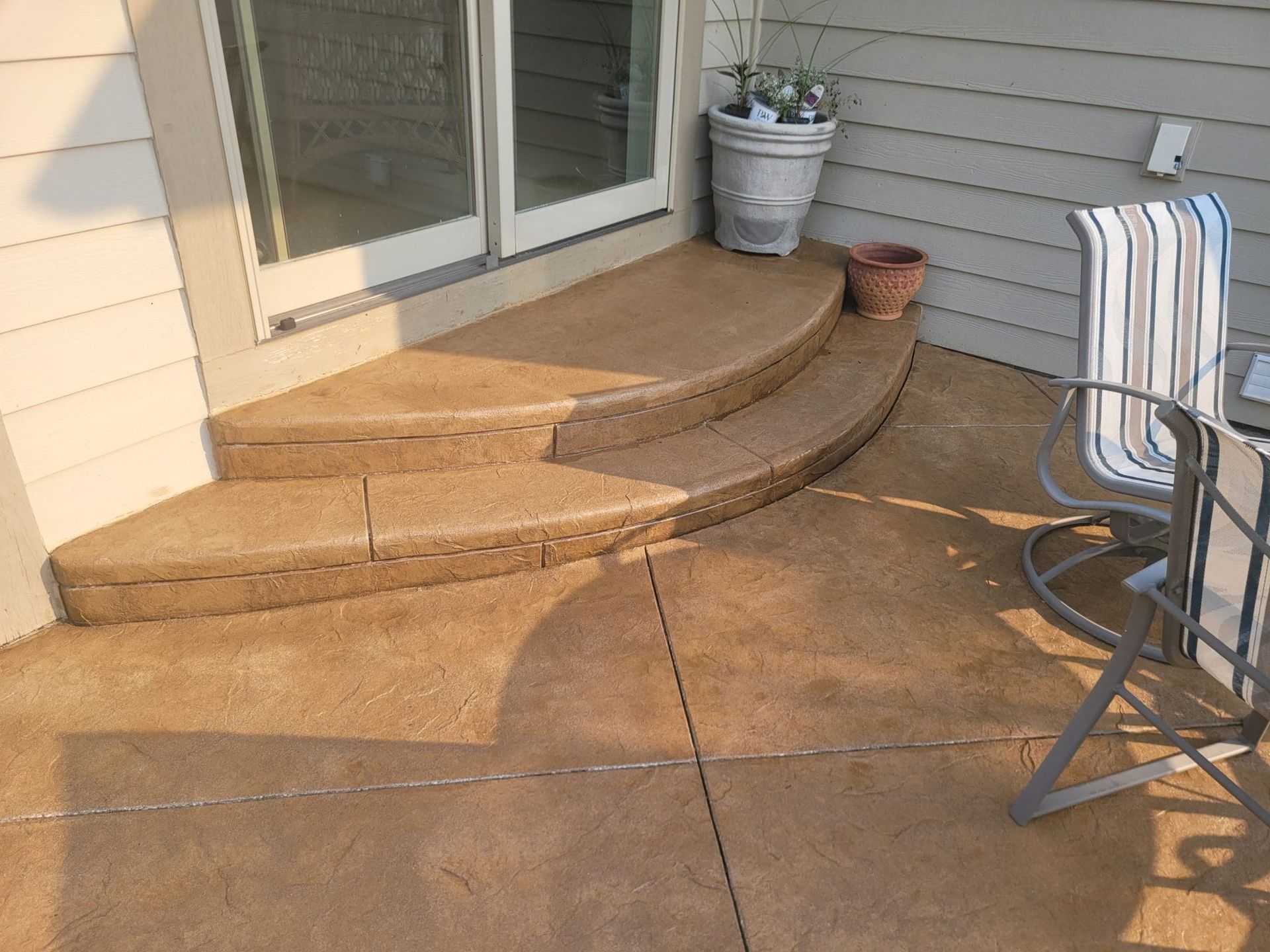 Patio with curved concrete steps leading to a sliding glass door and a potted plant beside the wall.