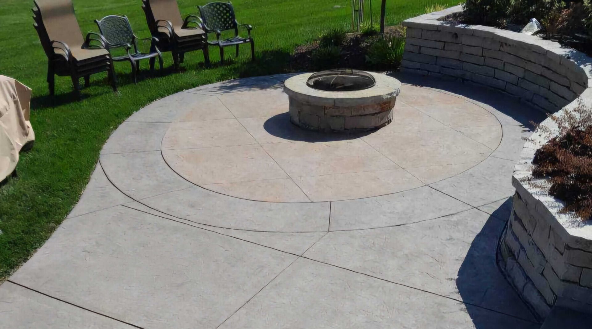 Backyard patio with circular stone fire pit, curved seating wall, and lawn chairs on grass