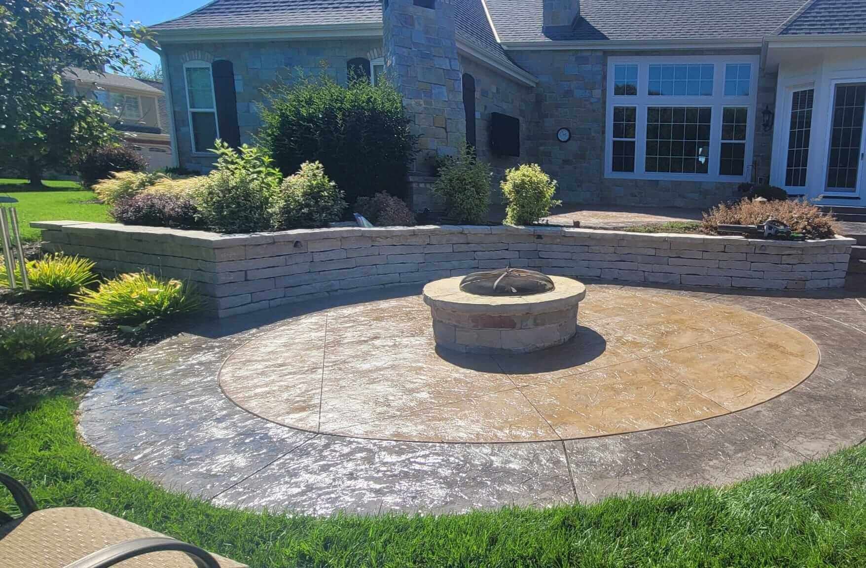 Backyard patio with circular stone fire pit and low retaining wall in front of a house