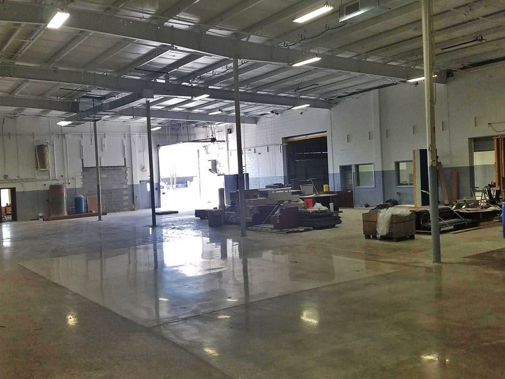 Empty industrial warehouse with concrete floor, metal beams, and bright open loading bay doors