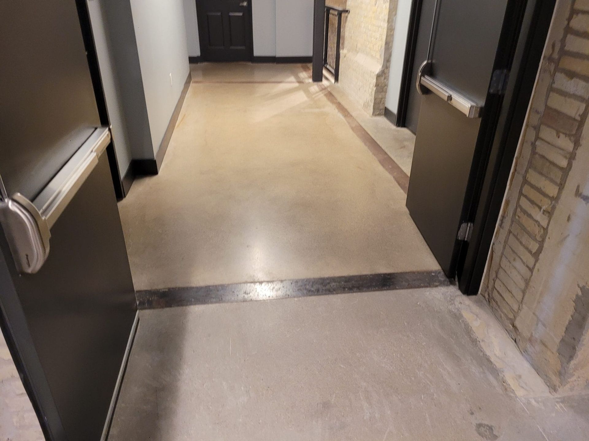 Empty indoor hallway with beige flooring, dark doorways, and a doorway threshold in the foreground