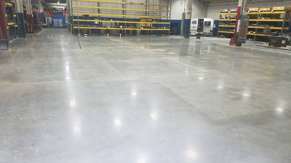 Empty industrial warehouse with a polished concrete floor and metal shelving in the background
