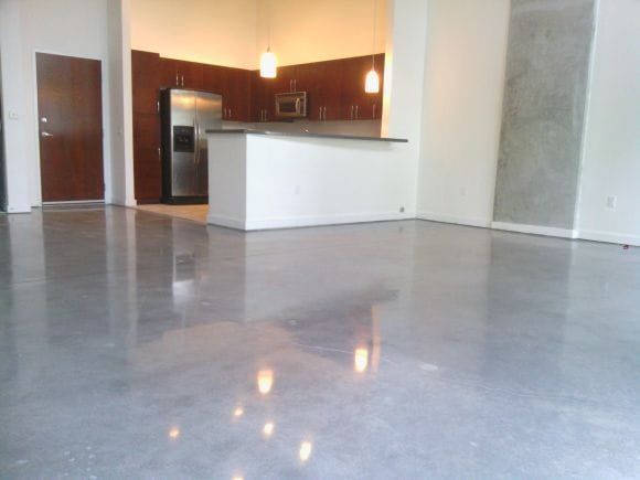 Empty modern kitchen and living area with polished concrete floors and white island counter