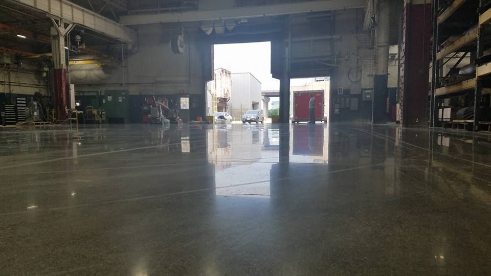 Empty industrial warehouse with a shiny concrete floor and a bright open doorway in the center.