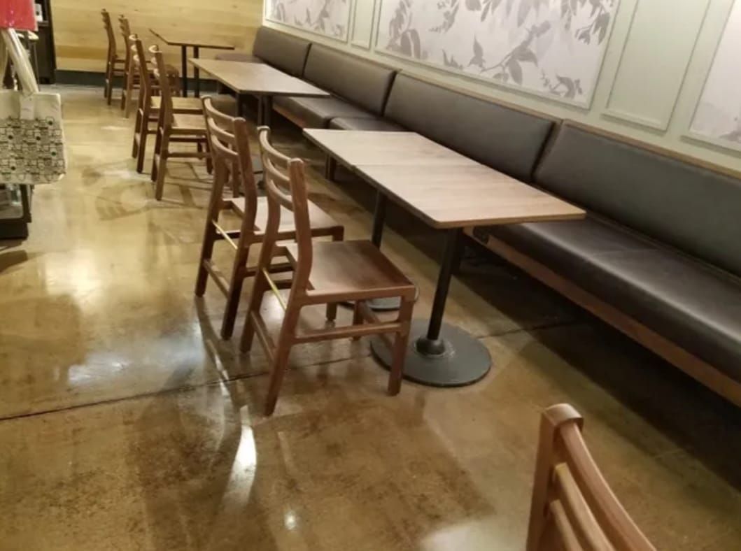 Empty restaurant seating area with wooden chairs, long tables, and a cushioned bench along the wall