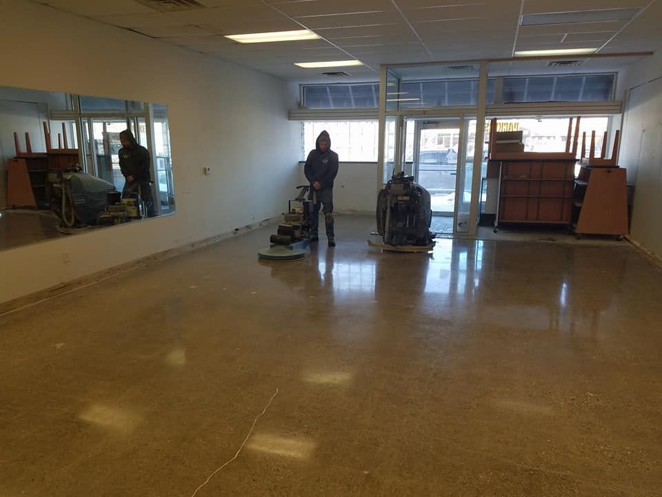 Empty room with polished floor, a person using a floor buffer, and windows at the far end