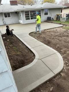 New concrete walkway curving through a yard, with workers smoothing the surface next to a house