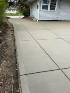 Fresh concrete walkway beside a white house and dirt yard