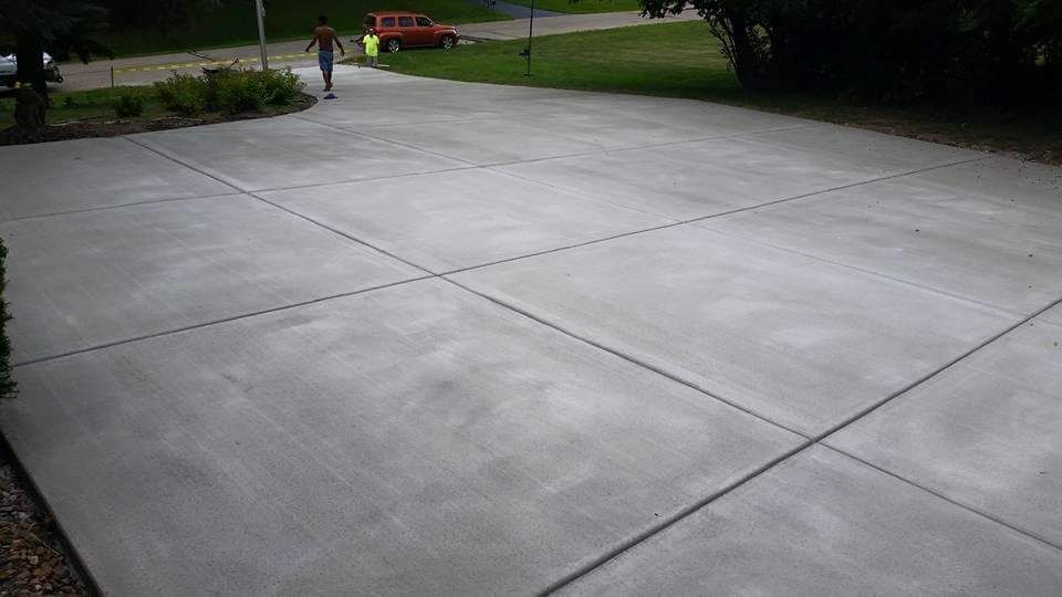 Empty concrete driveway beside a grassy yard, with a small red truck in the distance.