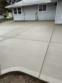 Concrete driveway beside a gray house, with a curved stone edge in the foreground.