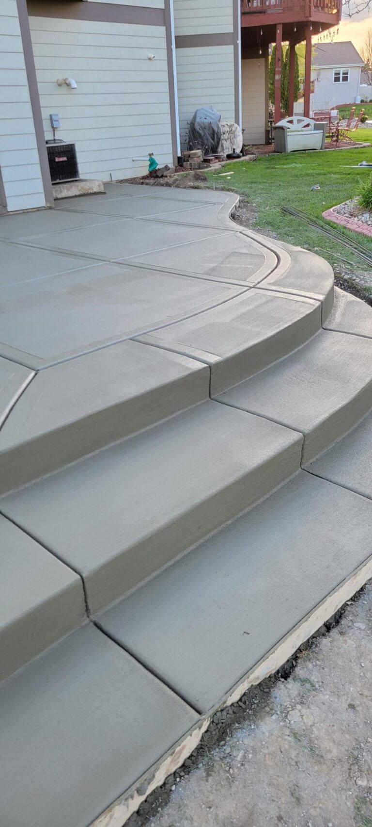 Concrete front steps and a curved walkway leading to a house entrance with a small garden.