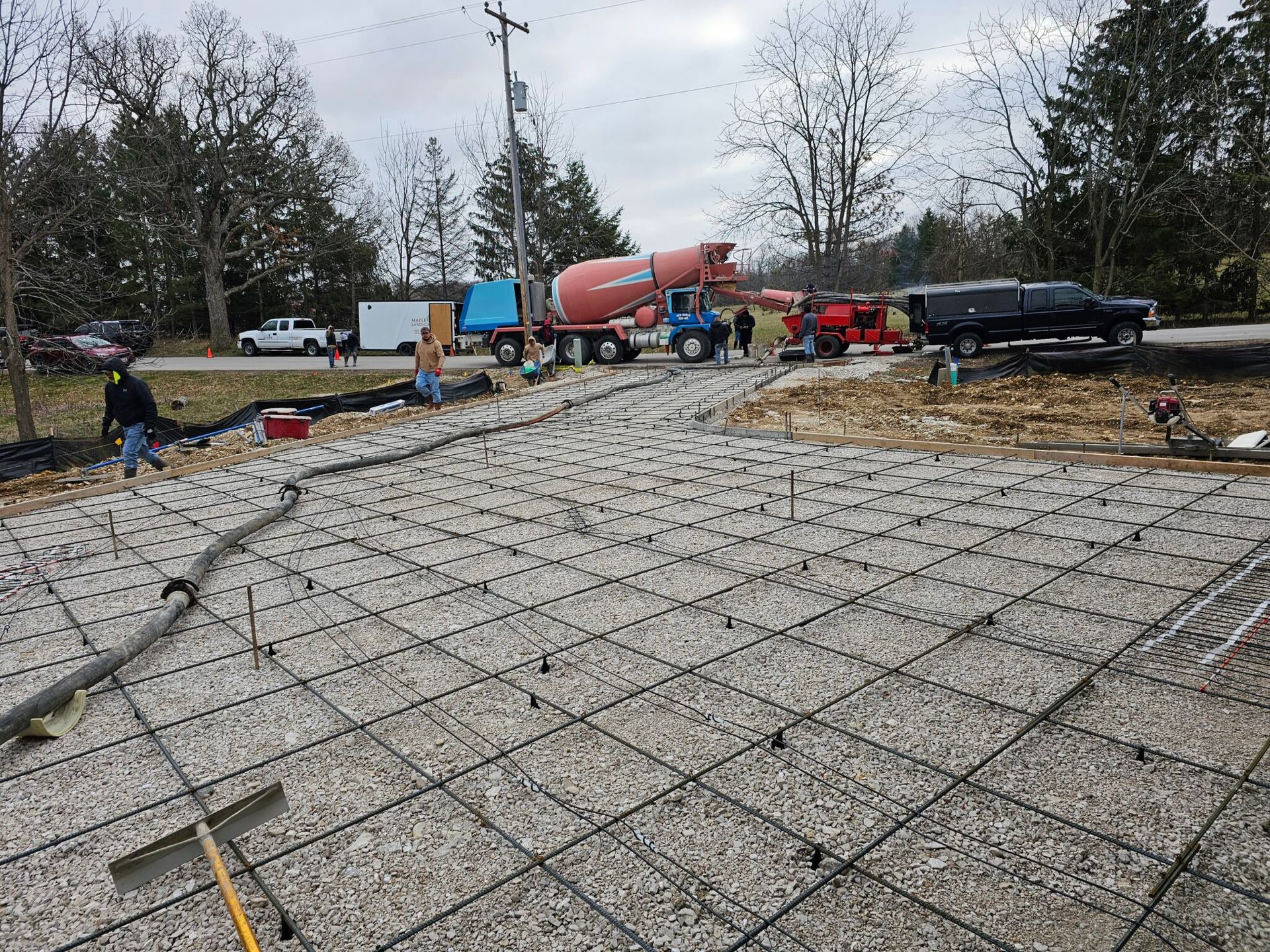 Concrete foundation site with rebar grid, workers, and cement trucks on an overcast day