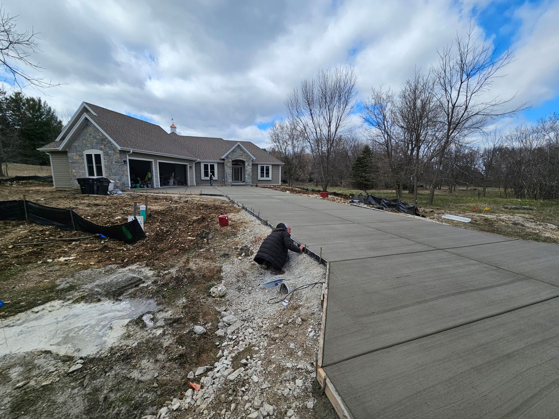 Suburban house with a long concrete driveway, patchy winter yard, and cloudy sky