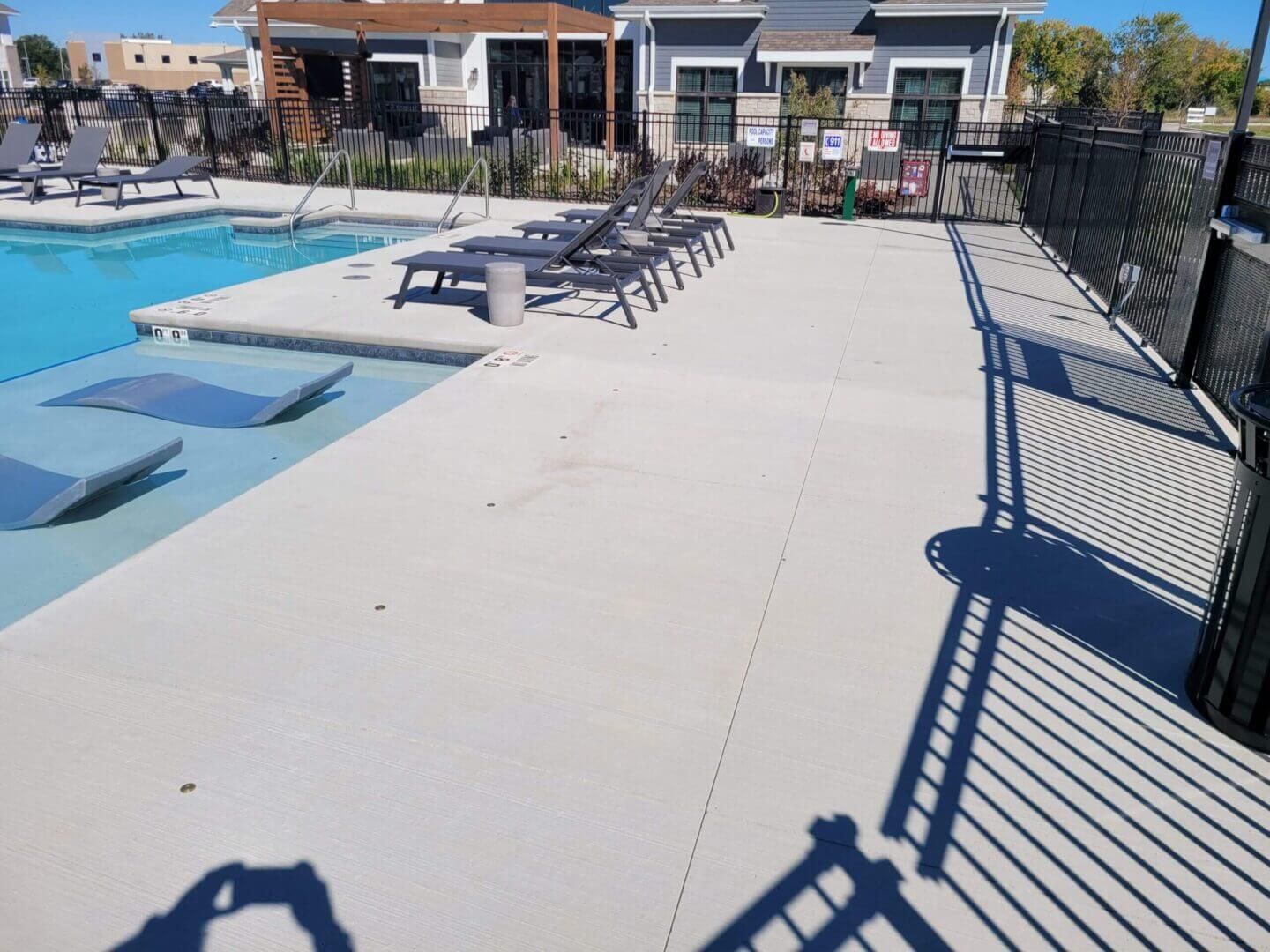 Poolside walkway with lounge chairs beside a swimming pool on a sunny day