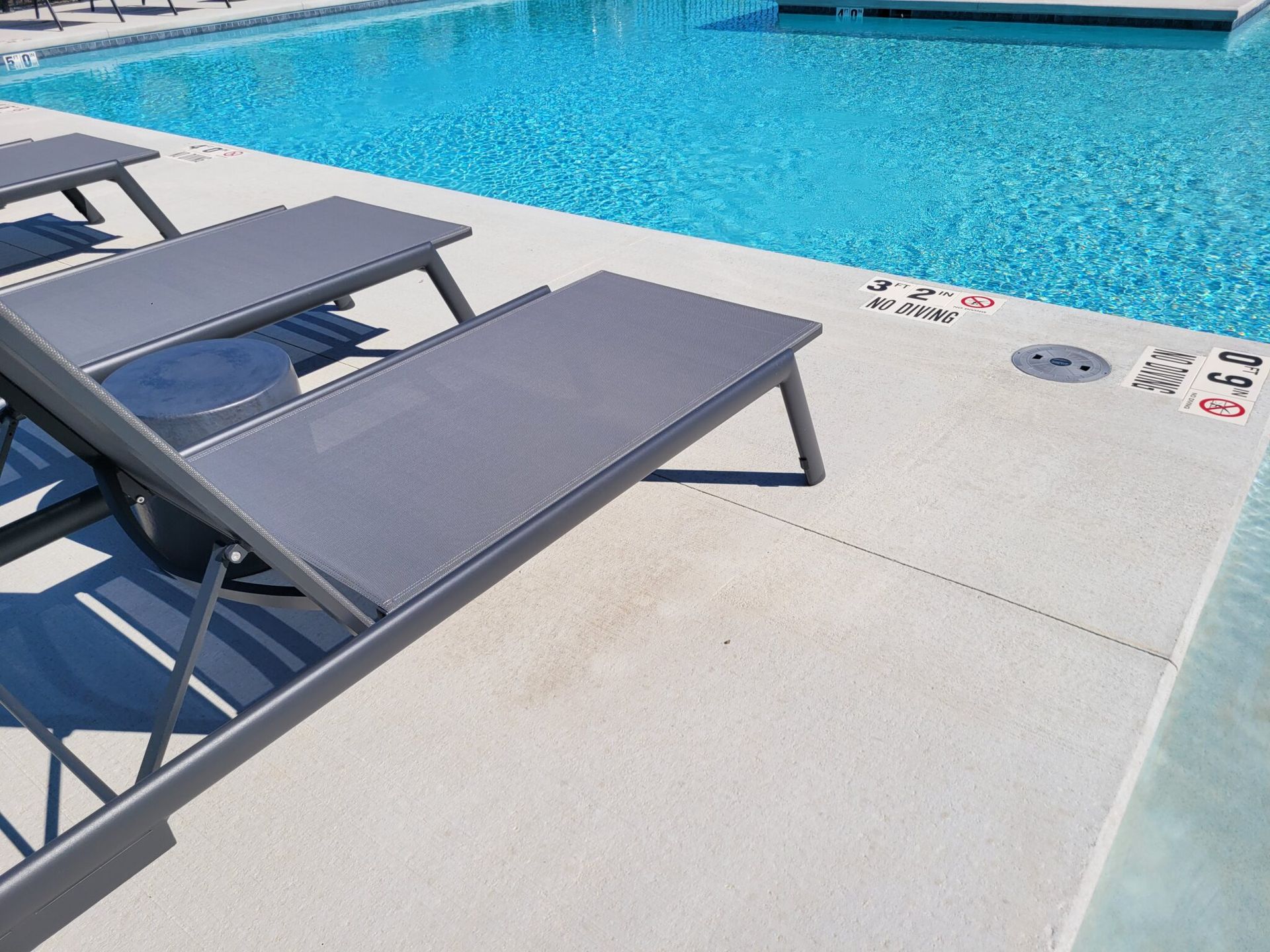 Poolside lounge chairs beside a bright blue swimming pool on a sunny day