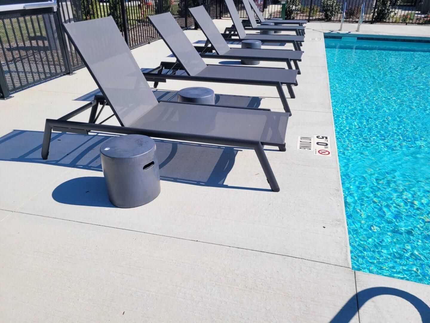 Poolside lounge chairs beside a bright blue swimming pool on a sunny deck
