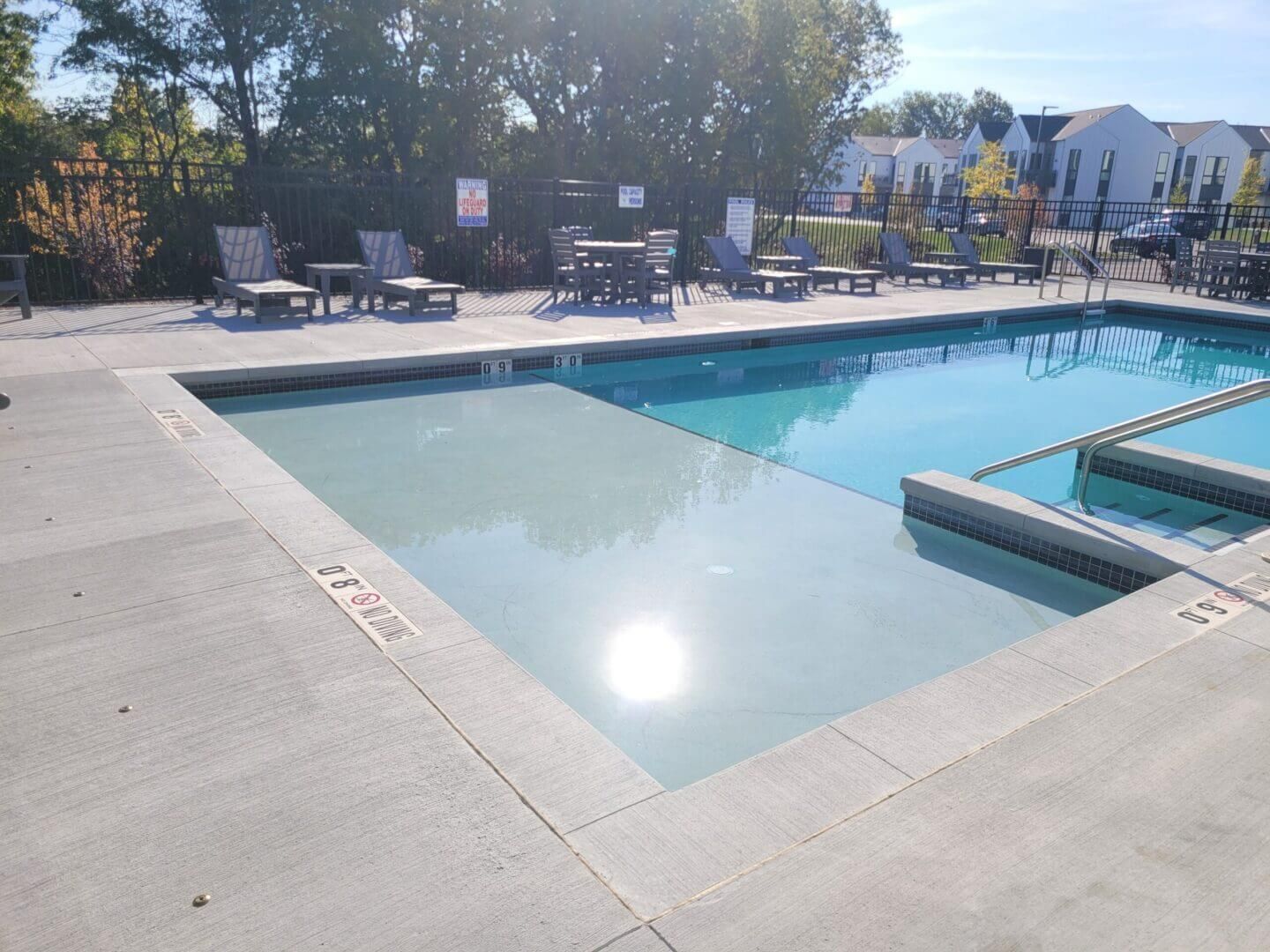 Outdoor swimming pool with lounge chairs, bright sunlight, and a shallow spa area