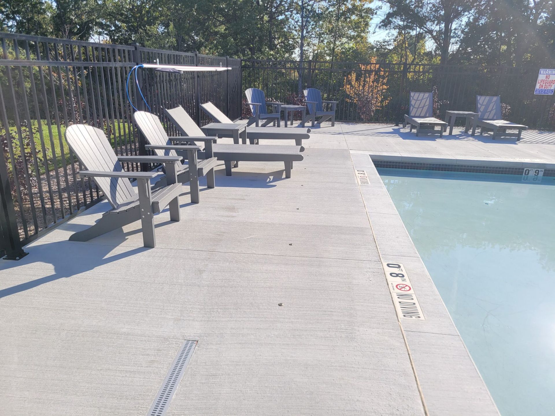 Outdoor pool deck with lounge chairs beside a swimming pool and fence.