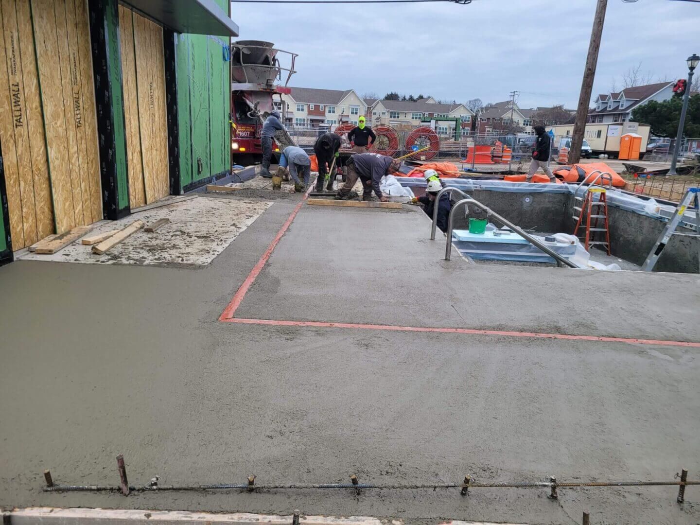 Construction site walkway with workers, concrete slabs, and orange safety barriers along a waterfront