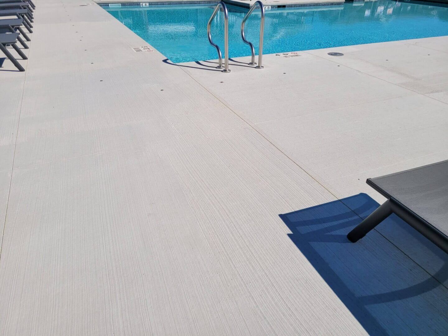 Poolside deck with a blue swimming pool, metal ladder, and gray lounge chair in the foreground.