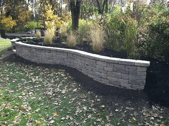 Curved gray stone retaining wall beside a grassy garden with trees and shrubs