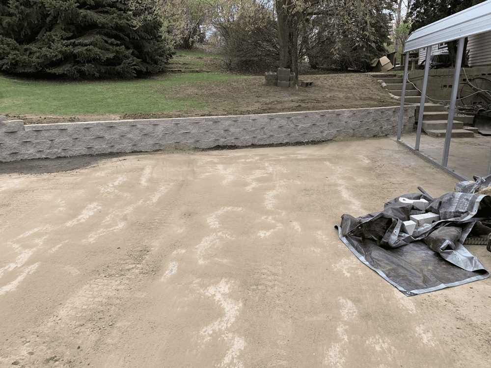 Concrete patio with a stone retaining wall and folded tarp beside a covered structure outdoors