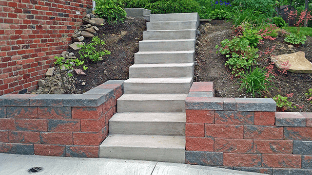Concrete steps leading up a landscaped brick retaining wall and garden beds